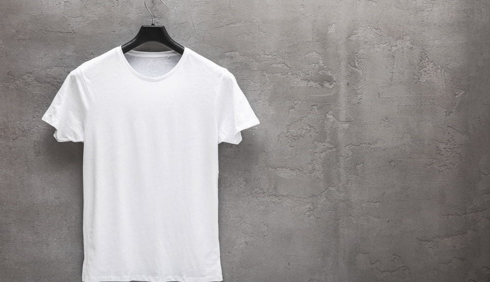 Front side of male white cotton t-shirt on a hanger and a concrete wall in the background. T-shirt without print and copyspace for your text on right side